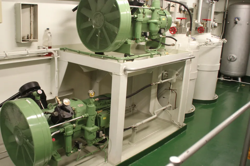 Two starting air compressors mounted on a two-tier frame in a ship engine room, with their air receivers alongside