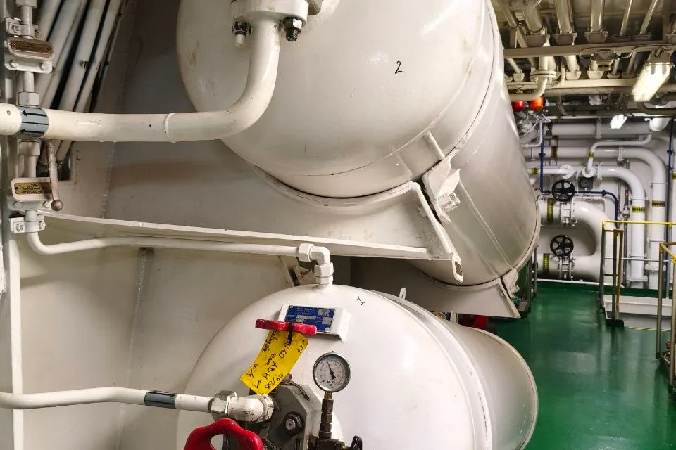 Two starting air receivers stacked in a ship engine room, with an isolating valve, pressure gauge and drain pipework at the head of the lower vessel