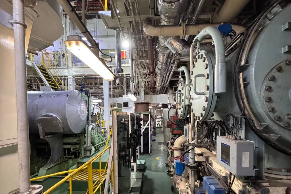 Side of a large marine main engine: a bolted oval crankcase inspection door with its handle, a large circular cover held by a ring of studs and nuts, and lagged pipework running past