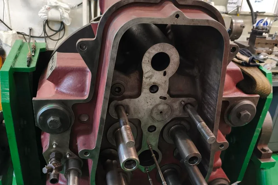 Marine engine cylinder head mounted on a green overhaul stand in a ship workshop, opened with valve guides and studs laid out