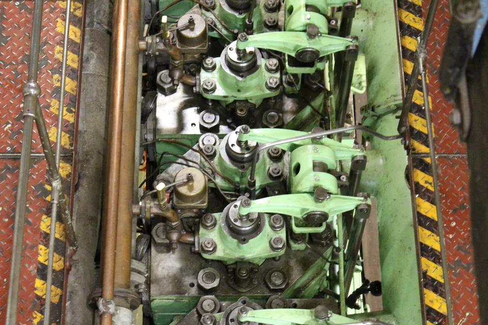 Cylinder heads on a ship's main engine with rocker arms and valve gear exposed, injector lines and copper piping running along the engine top