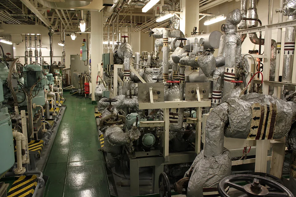 A row of pump sets with electric motors along one side of a ship engine room, insulated fuel heater module opposite