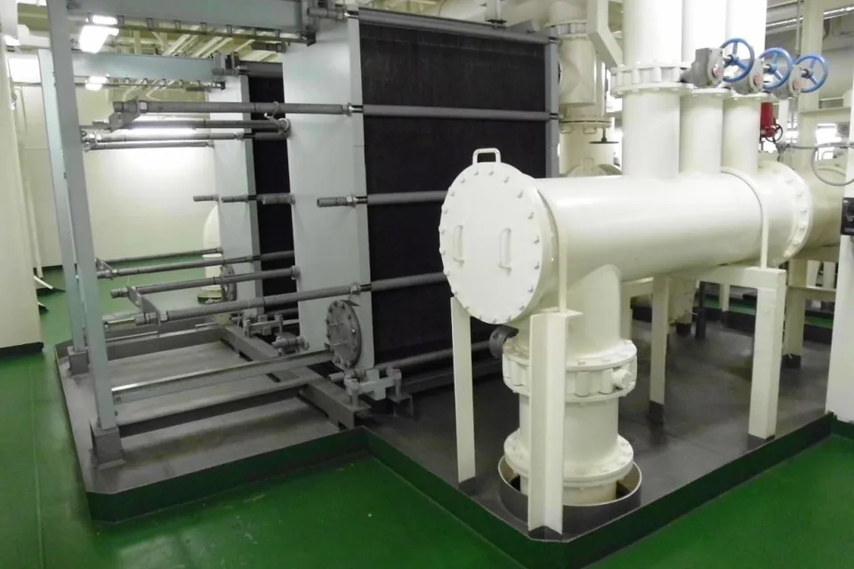 Plate heat exchanger for jacket cooling water in a container ship engine room, tie bars and plate pack beside a sea water strainer and large-bore flanged piping