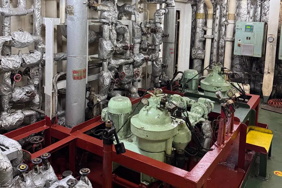 Two centrifugal separators with their motors on a red bedplate in a ship engine room, surrounded by lagged feed and heater pipework, with a control cabinet on the bulkhead behind
