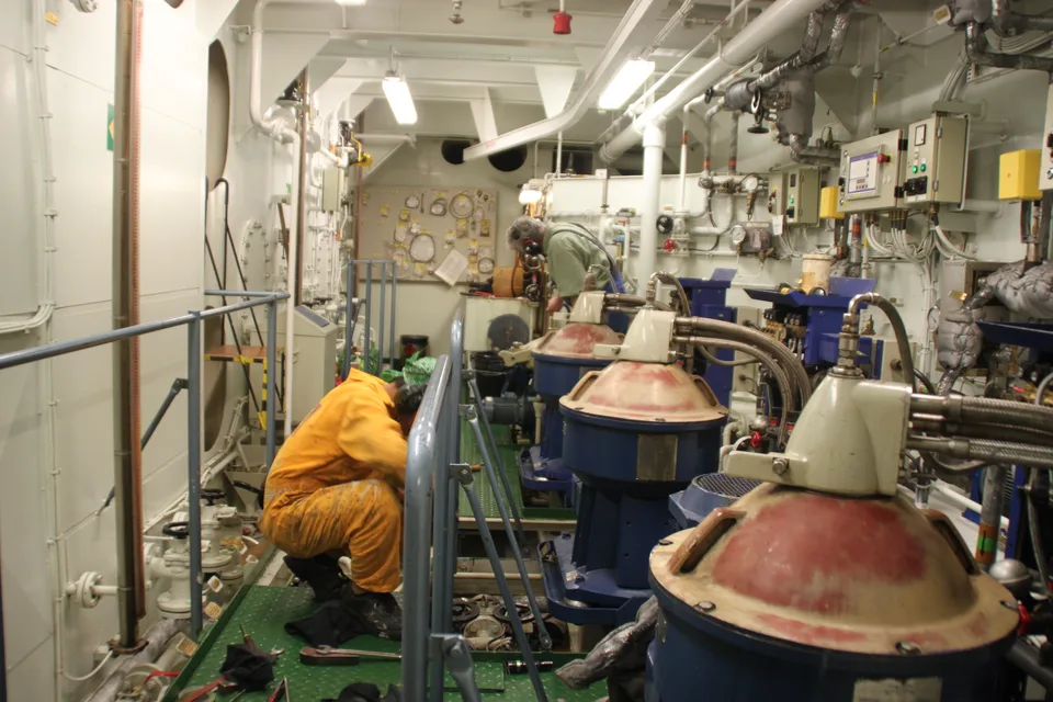 Three disc-stack separators in a ship separator room, bowl hoods stained by heavy fuel oil, control panels on the bulkhead behind