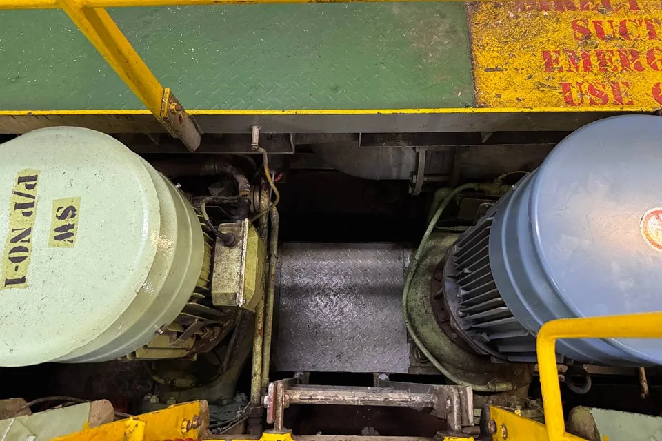 Two motor-driven pumps seen from the walkway grating above, the left motor end cover stencilled SW P/P NO-1, with an emergency direct-suction marking stencilled on the deck edge overhead