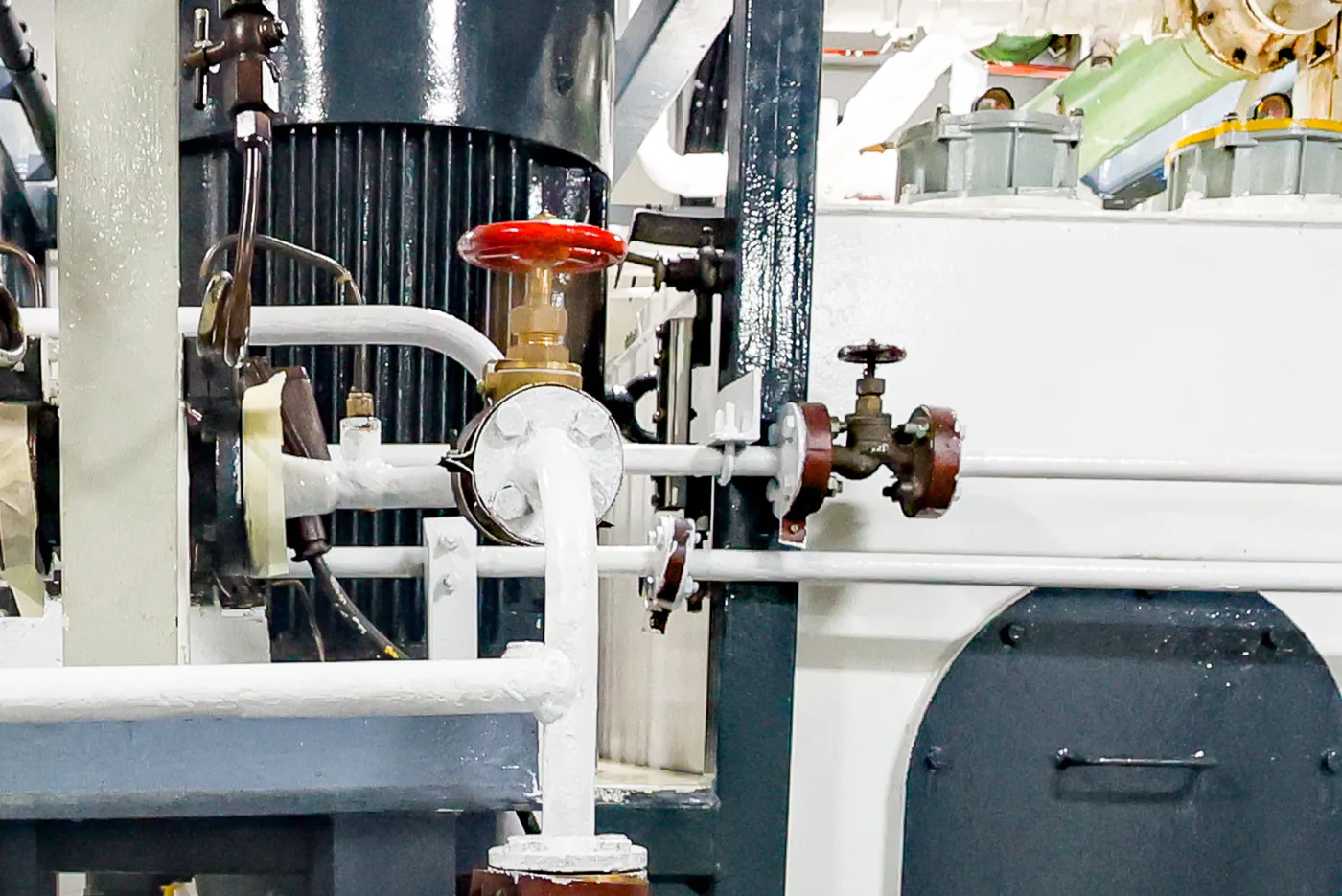 Marine globe valves with red handwheel on white engine-room piping