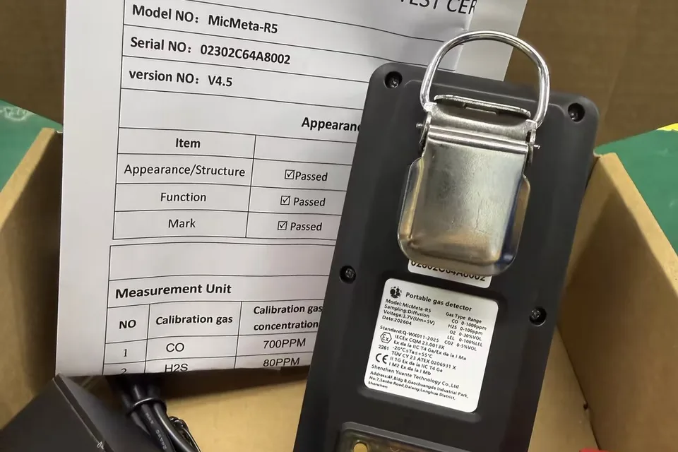 Portable multi-gas detector beside its printed test certificate, showing model, serial and version numbers, passed appearance, function and mark checks, and a calibration gas table