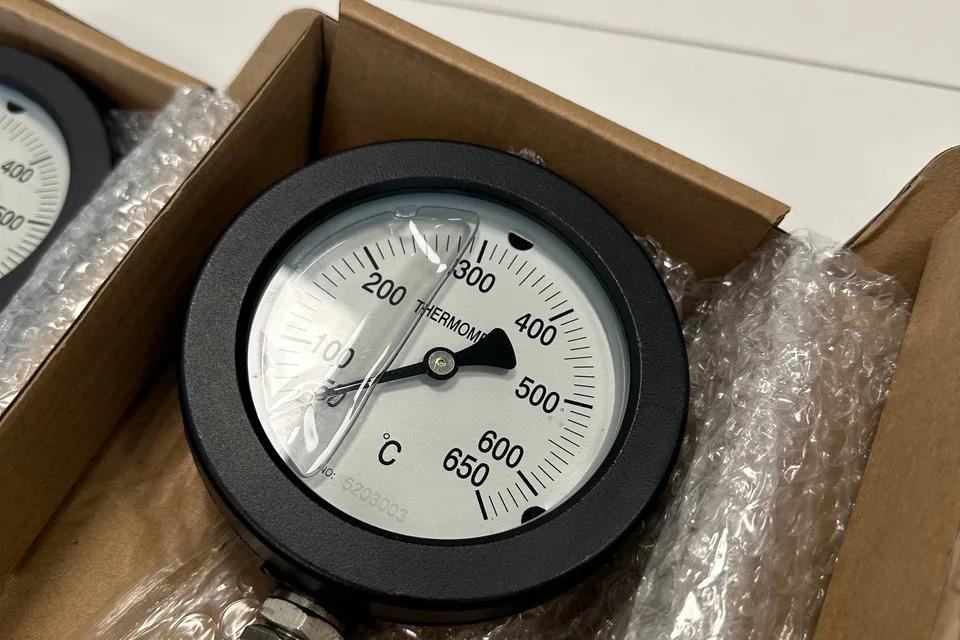Bimetal dial thermometer with a 0 to 650 degree Celsius scale and a stamped serial number, packed in a box with its stem and union fitting